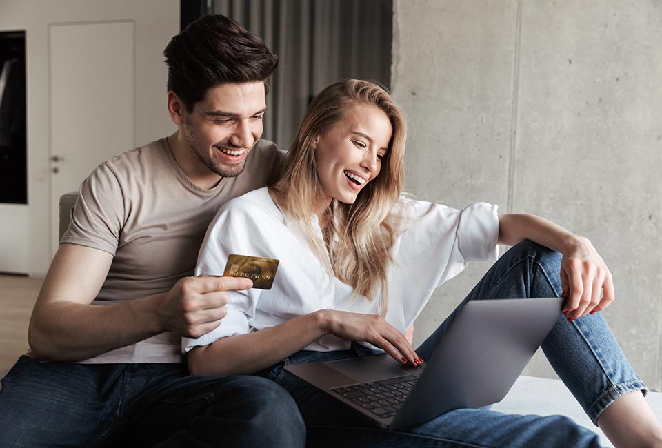 Photo of young happy loving couple in home indoors on sofa using laptop computer holding credit card.